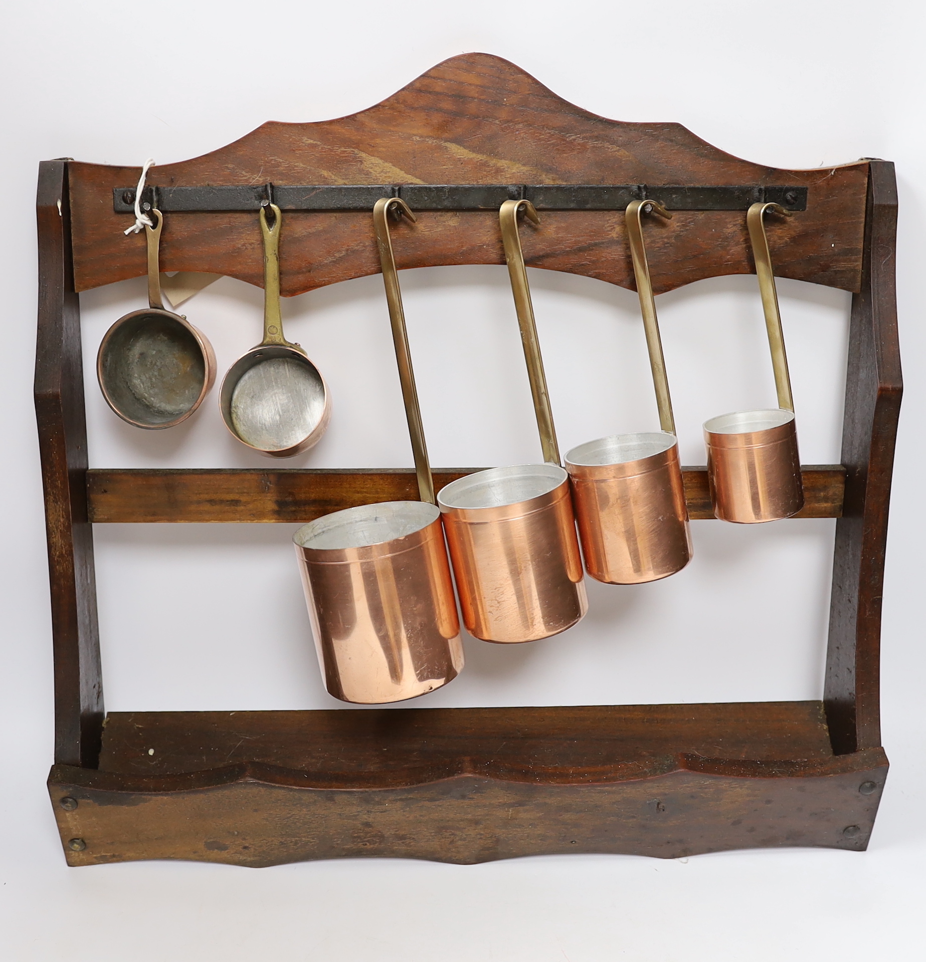 Two small copper sauce pans, four graduated copper measuring pans and a hanging rack, largest 47cm wide